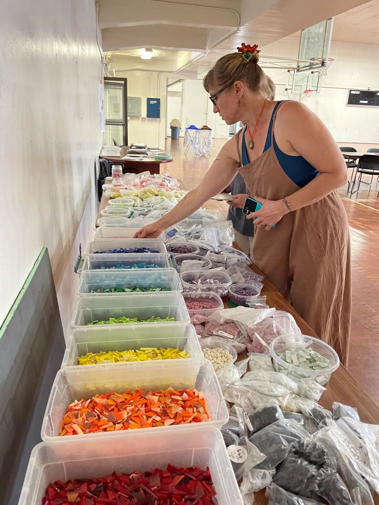 middle aged blonde white lady showing someone a selection of colorful glass pieces for mosaic